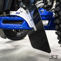 Close-up of a blue off-road vehicle’s suspension and large rugged tire, featuring S3 Power Sports 2018+ Polaris Rzr Xp Turbo S Trailing Arm Guards with black mud flaps on a metal bracket labeled S3. The ground beneath is light-colored and smooth.