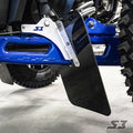 Close-up of a blue off-road vehicle’s suspension and large rugged tire, featuring S3 Power Sports 2018+ Polaris Rzr Xp Turbo S Trailing Arm Guards with black mud flaps on a metal bracket labeled S3. The ground beneath is light-colored and smooth.