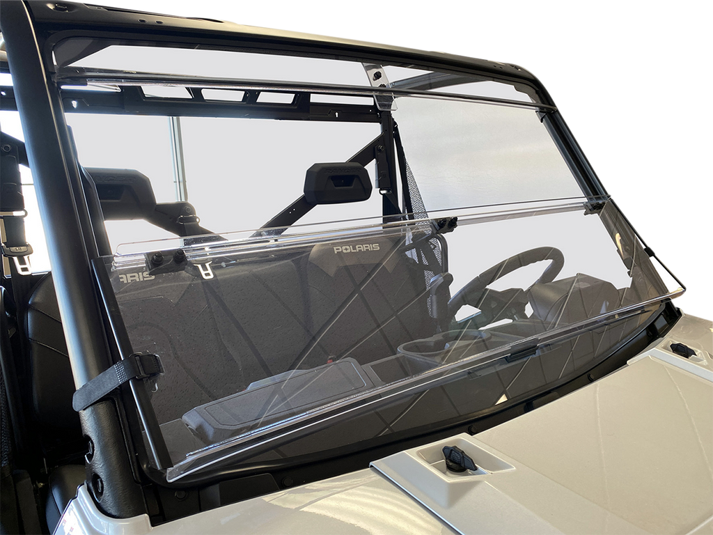 A clear, two-panel windshield is installed on a Polaris off-road vehicle. The windshield is slightly open at the center and attached to the vehicle’s black frame. The seats and interior details are visible through the glass. The background is plain and wh