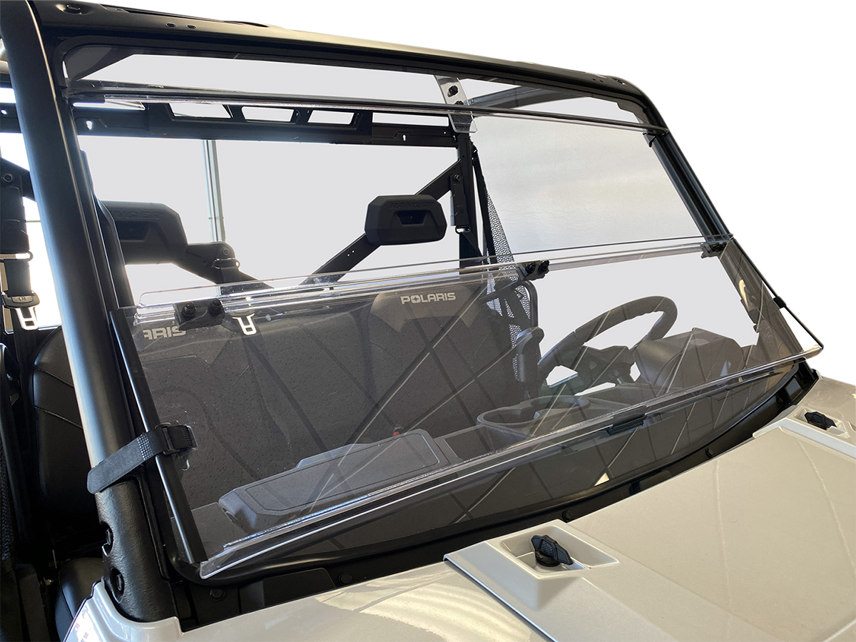 A clear, two-panel windshield is installed on a Polaris off-road vehicle. The windshield is slightly open at the center and attached to the vehicle’s black frame. The seats and interior details are visible through the glass. The background is plain and wh