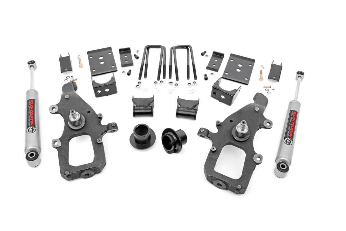 A Lowering Kit | 3 Inch FR | 5 Inch RR | Ford F-150 2WD (2004-2008) is displayed on a white background, featuring two large black spindles, silver shock absorbers, U-bolts, brackets, bushings, and assorted hardware.
