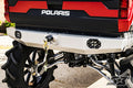 Close-up of the S3 Power Sports 2013-2020 Polaris Ranger Rear Winch Bumper on a red Polaris off-road vehicle, showing its silver finish, black end caps and mounting brackets, a tow hook with chain, deep-treaded tires, and exposed suspension parts.