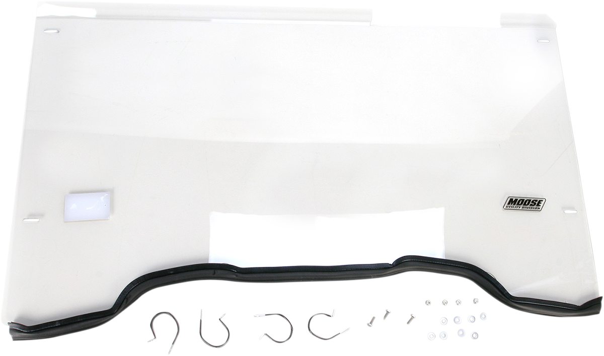 A clear, rectangular plastic windshield with a black rubber edge at the bottom. The Moose Utility Division logo appears on the lower right. Below the windshield are metal mounting brackets, screws, washers, and other small hardware pieces laid out on a wh