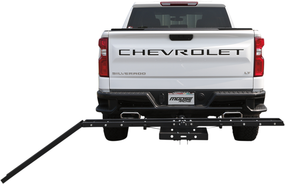 A white Chevrolet Silverado LT pickup truck is seen from behind. Attached to the trailer hitch is a black metal rack with an extended arm angled downward, likely for transporting items such as bikes or scooters. The vehicle is parked against a plain white
