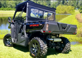 A CFMoto UForce 1000 with a Sliding Glass Rear Window is parked on green grass near a pond, surrounded by trees and bushes under a sunny sky, showcasing its cargo bed, suspension, and rugged utility features.