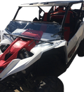 A white and red off-road utility vehicle with a clear windshield, black roof, and red seats. The Yamaha logo is visible on the side, and the vehicle is shown from the front left angle, highlighting its rugged design and suspension system.