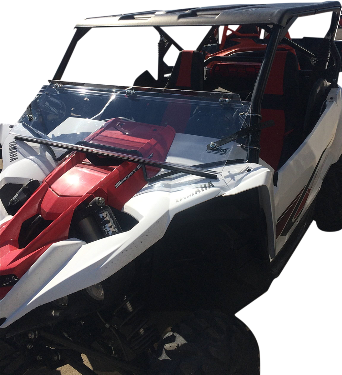 A white and red off-road utility vehicle with a clear windshield, black roof, and red seats. The Yamaha logo is visible on the side, and the vehicle is shown from the front left angle, highlighting its rugged design and suspension system.