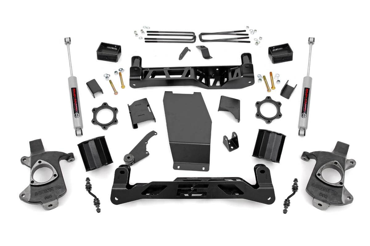 The 5 Inch Lift Kit (Alum/Stamp Steel, V2) for Chevy/GMC 1500 (14-18) is displayed on a white background, featuring black or metallic gray brackets, shock absorbers, spindles, U-bolts, skid plates, hardware, and spacers arranged neatly.