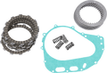A motorcycle clutch kit with friction plates, steel plates, coiled springs, and a teal gasket, all neatly arranged on a white background. The friction and steel plates are stacked, and the small springs and flat gasket are placed separately.