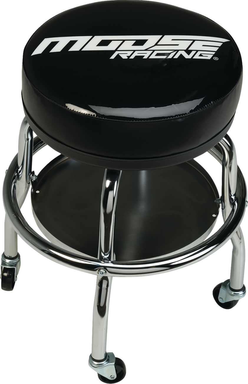 A black round stool with Moose Racing written in white on the cushioned seat. The stool has chrome legs, four swivel casters, and a circular lower shelf connecting the legs. The design is sturdy and industrial, ideal for a garage or workshop.