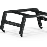 The 2005+ Toyota Tacoma Treck 5Ft. Bed Mid-Size Truck Adjustable Bed Rack System in textured black features angular metal legs, crossbars, perforated side holes for attachments, a ROAD ARMOR logo, and includes a bracket kit. Plain white background.
