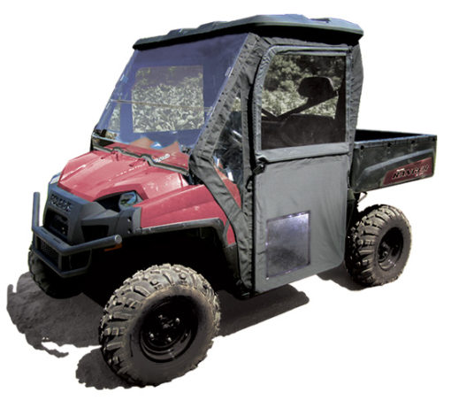 A Polaris Ranger Full Size with round tubes and steel framed full doors, in red, featuring large rugged tires and a black cab enclosure with clear plastic windows, is parked on a light surface with its vehicle bed visible at the back.