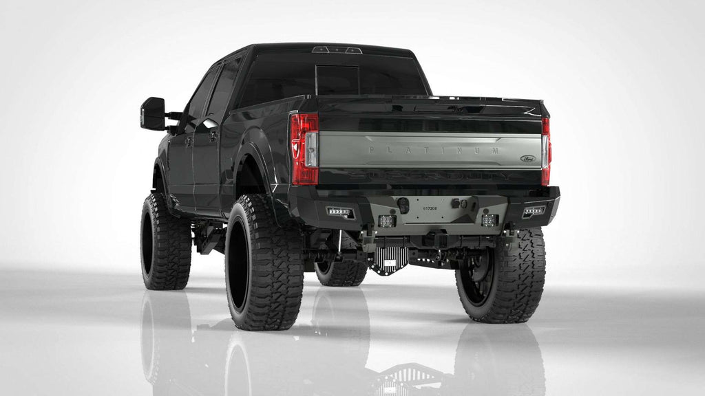 A lifted black 2017-2021 Ford F-250 with extra-large off-road tires and wide fender flares is shown from the rear left, featuring a metallic silver PLATINUM tailgate and an Identity Rear Bumper Full Kit with center section and accent lights.