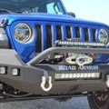 Close-up of a blue Jeep JL Rubicon with a Stealth Front Winch Bumper (Full Width, Texture Black) featuring a sheetmetal bar guard, Warn Powerplant winch hook, D-ring shackles, LED light bars, round headlights, and seven-slot grille.