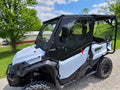A white Honda Pioneer 1000 side-by-side with Offroad Armor Aluminum Upper Doors and a black roof is parked on gravel near green grass and trees under a blue sky with scattered clouds, with a barn visible in the background.
