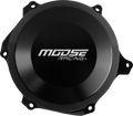 A round, black motorcycle engine cover with the text MOOSE RACING in bold white letters at the center. The metal cover has a ridged, circular pattern and four mounting holes around the edges. The background is plain and light-colored.