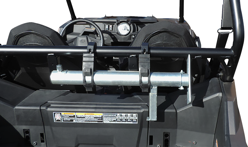 A metal fire extinguisher mount is attached to the horizontal roll bar behind the seats of an off-road utility vehicle. The dashboard, black seats, and control panel with a round gauge are visible in the background. Warning labels are on the rear panel.