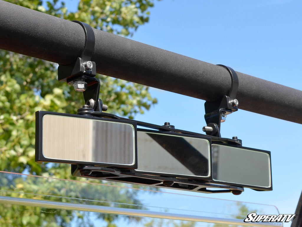 The 3 Panel Rear View Mirror with 1.75 Clamps is mounted on a horizontal roll bar with two adjustable brackets. Trees and a clear blue sky can be seen in the background, and the SuperATV logo appears in the bottom right corner.