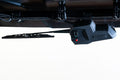A close-up view of the Seizmik UTV Windshield & Headlight Wiper Washer Kit installed on a vehicle, showing its black housing with a green light, red button, visible cables, and mounting hardware.