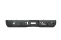 A front view of the 2015-2019 GMC/Chevy 2500 Stealth Rear Winch Bumper in texture black, featuring angular corners, mounting holes, a central winch opening for Warn M8000 or 9.5XP, and a white Road Armor logo on the lower right. White background.