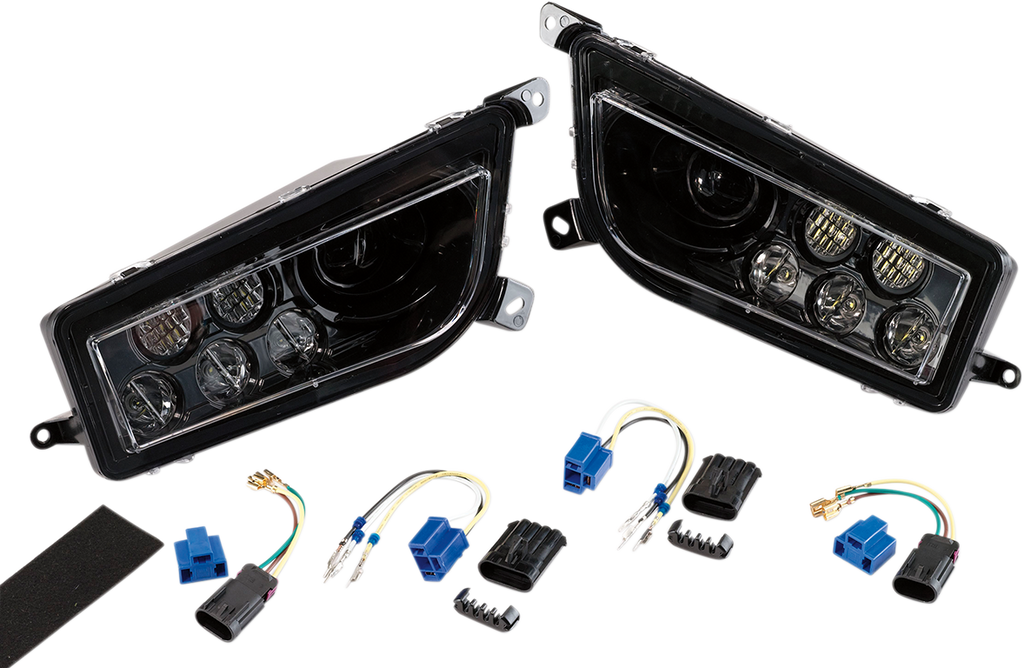 Two black automotive headlight assemblies with clear lenses are shown side by side. Below them are wiring harnesses, blue and black electrical connectors, and a strip of adhesive foam, all laid out on a white background.