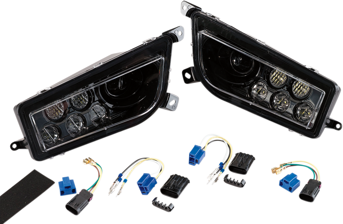 Two black automotive headlight assemblies with clear lenses are shown side by side. Below them are wiring harnesses, blue and black electrical connectors, and a strip of adhesive foam, all laid out on a white background.