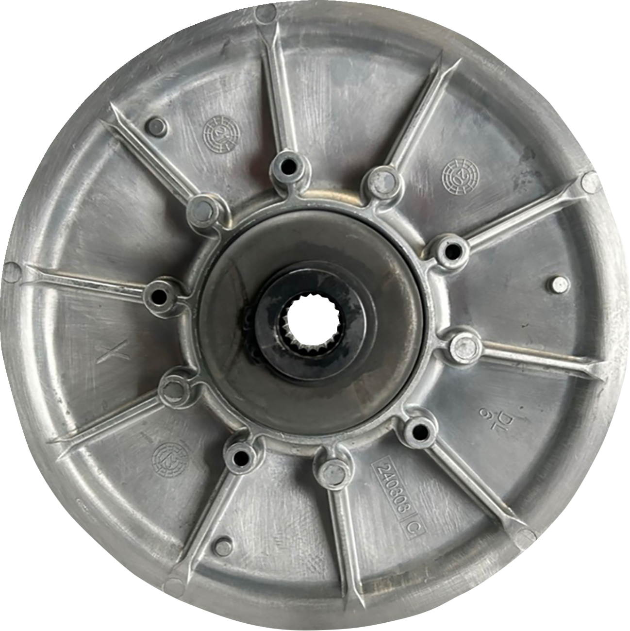A metallic circular mechanical component with radial spokes, a central hole containing gear-like teeth, and several smaller holes around the center. The surface has numbers, letters, and embossed markings, suggesting it is a part of a machine or vehicle.