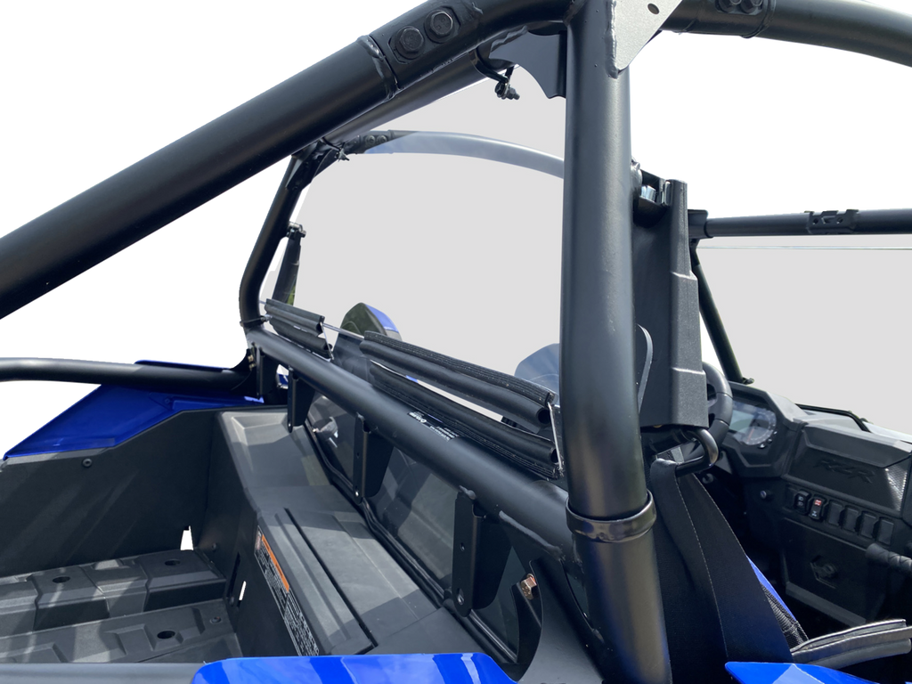Close-up view of a blue off-road vehicle’s interior, focusing on its black tubular roll cage and safety net. The dashboard, steering wheel, seats, and rear storage compartment are visible, all under bright lighting against a white background.