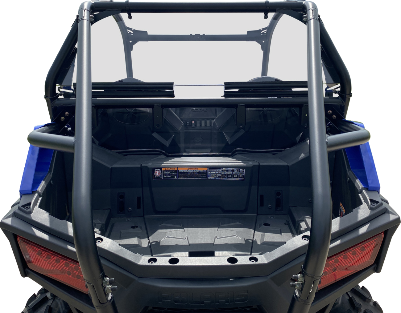 Rear view of an off-road utility vehicle with an empty cargo bed, tubular roll cage, two rear red tail lights, and a dashboard with visible warning stickers and controls. The vehicle features a sturdy, rugged design, and the image background is white.