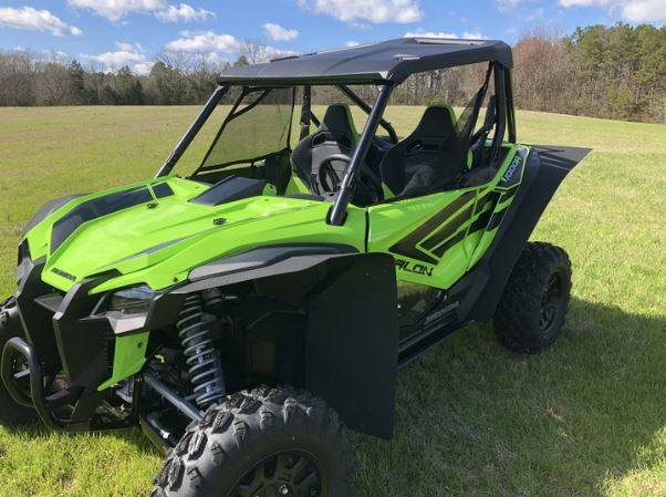 A Honda Talon 1000X-4 equipped with Trail Armor Mud Flap Fender Extensions is parked on grass under a blue sky, showcasing its large tires, black roof, open sides, and the “Talon” name on its side with trees in the background.