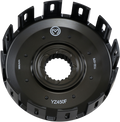 Close-up view of a black motorcycle clutch basket with evenly spaced rectangular slots around the edge, a splined central hole, and white markings including “YZ450F” and manufacturing codes. The surface is matte with a circular metal logo near the top.