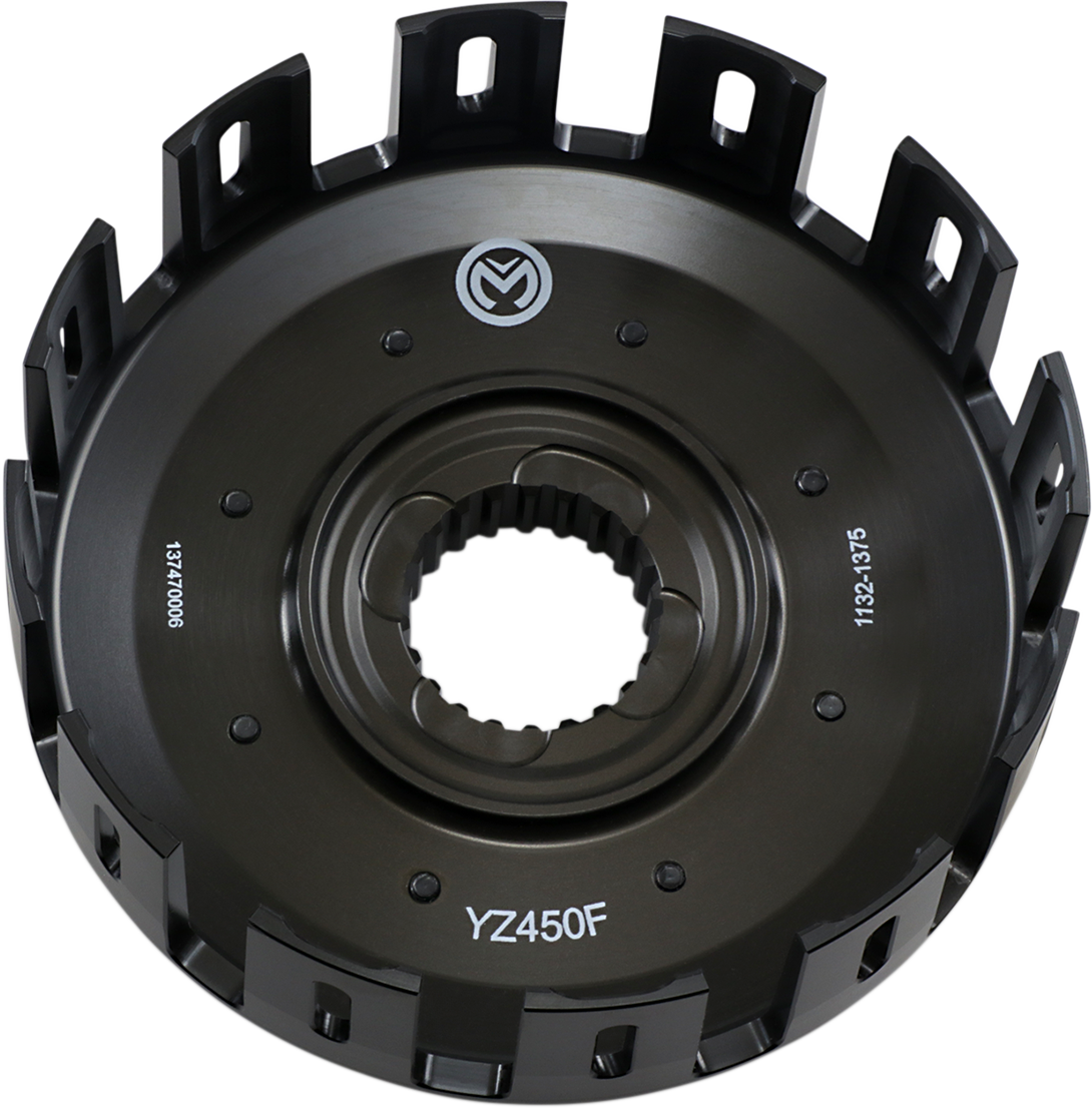 Close-up view of a black motorcycle clutch basket with evenly spaced rectangular slots around the edge, a splined central hole, and white markings including “YZ450F” and manufacturing codes. The surface is matte with a circular metal logo near the top.