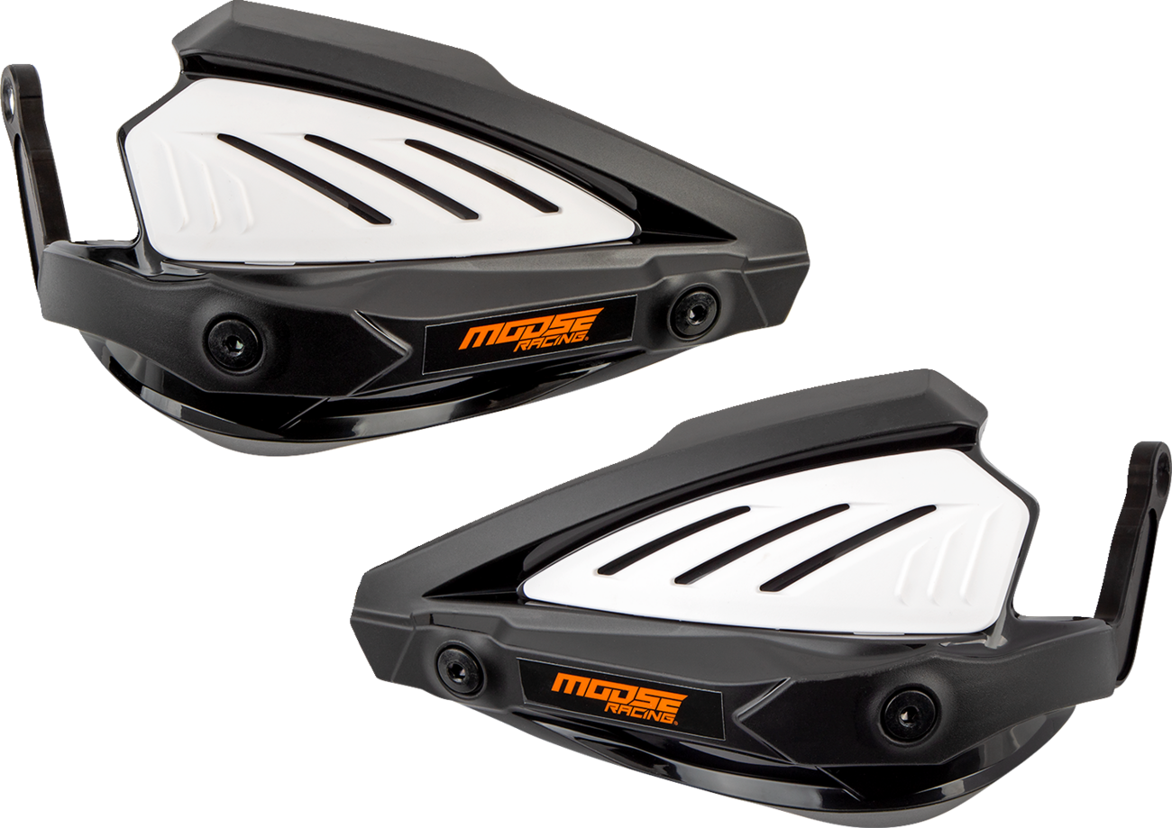 Two black and white plastic motorcycle handguards with angular designs, vented white panels, and orange Moose Racing logos are shown side by side on a light gray background. The handguards have mounting points and aerodynamic features.