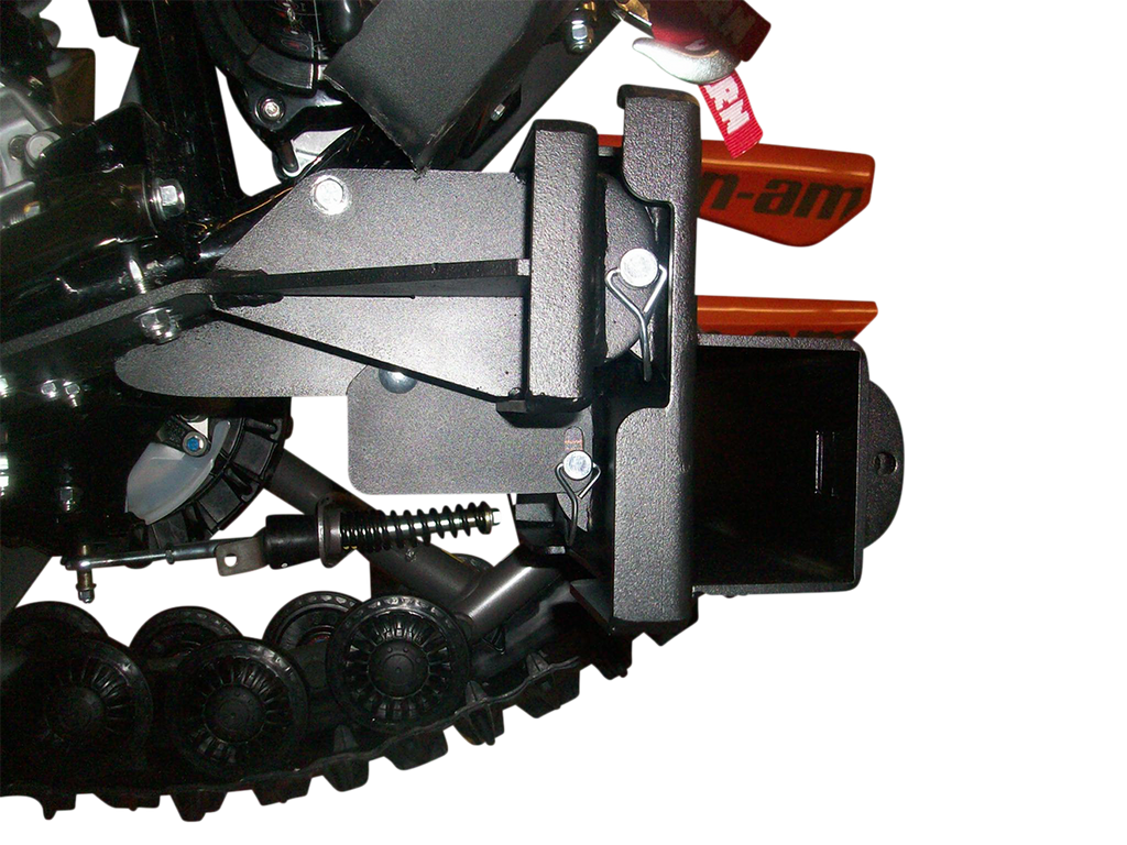 Close-up view of a mechanical component with a black metal bracket, bolts, spring, and part of a rubber track system. An orange part labeled Can-am is partially visible in the background, with a white background behind the machinery.