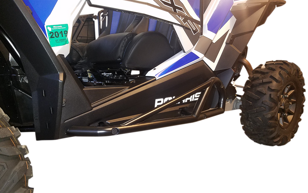 Close-up view of the side of a blue and white off-road vehicle with large rugged tires, black metal side rock slider bars for protection, and the word “Polaris” visible on the side panel. A green 2019 permit sticker is also attached near the front.