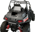 Rear view of a black off-road Polaris vehicle with red suspension springs, rugged tires, a roll cage, and open cargo space. The Polaris logo is visible, and red taillights are illuminated. The setting is a plain, light background.