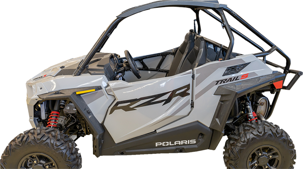 A silver Polaris RZR Trail S side-by-side off-road vehicle with black roll cage, rugged tires, and red suspension springs, viewed from the left side. The door features bold black RZR graphics and the word Polaris appears near the bottom.