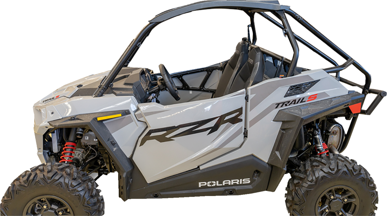 A silver Polaris RZR Trail S side-by-side off-road vehicle with black roll cage, rugged tires, and red suspension springs, viewed from the left side. The door features bold black RZR graphics and the word Polaris appears near the bottom.
