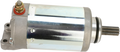 A metallic cylindrical starter motor with a shiny silver body, a terminal bolt with a red washer on top, mounting holes on the left end, and a protruding gear shaft on the right end, all set against a plain white background.