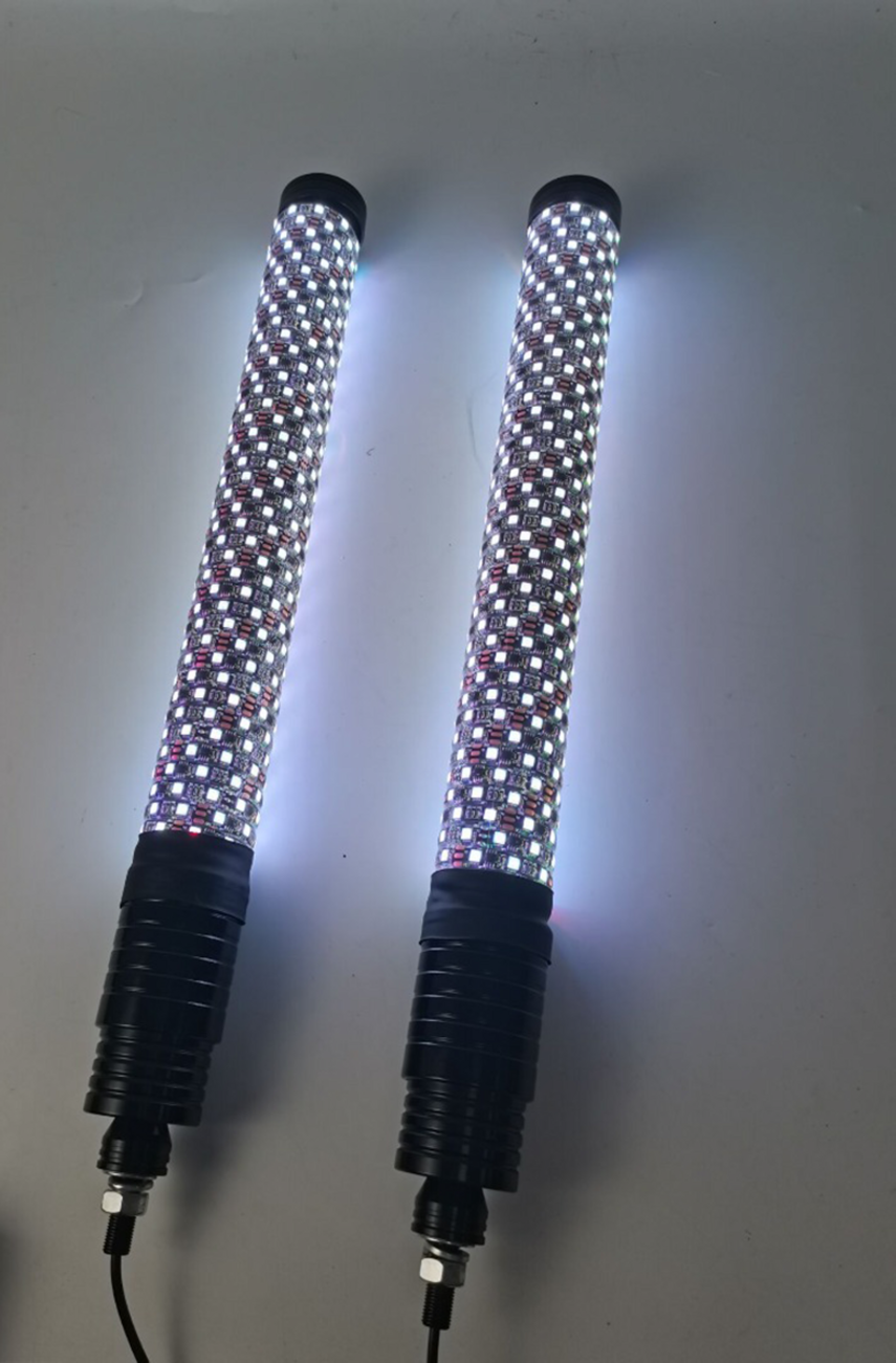Two cylindrical LED light wands emit bright white light. Each wand has a grid-like surface of illuminated individual LEDs and a black ribbed handle with attached power cords, all set against a plain, light gray background.