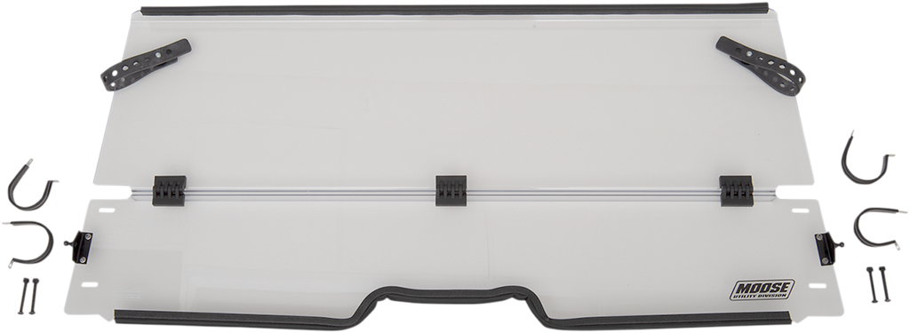 A clear, rectangular windshield with black mounting brackets and hardware pieces arranged around it. The windshield has a slight notch at the lower center and a Moose Utility Division logo in the bottom right corner. Two black adjustable arms are attached