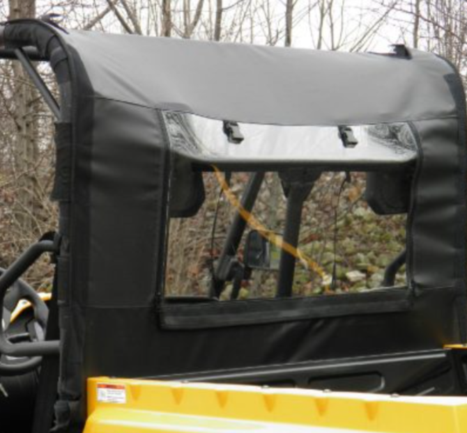 A close-up of the HiSun 500/700 – Soft Back Panel shows its black soft top and clear plastic rear window installed on a yellow off-road utility vehicle, with the roll cage, driver’s seat, trees, and rocks visible in the background.