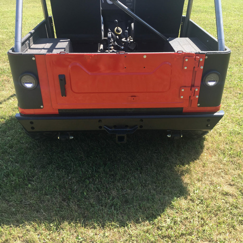 Close-up of a Mahindra Roxor Rear Bumper W/ Receiver on an open-top vehicle. The red tailgate, black panels, and two round taillights per side are visible as the vehicle sits on green grass with sunlight casting shadows.