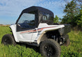 A Yamaha Wolverine RMAX 1000 with a Door/Rear Window Combo in white, featuring black wheels and a black soft cab, is parked on tall green grass with mud on its tires, set against trees and a blue sky.