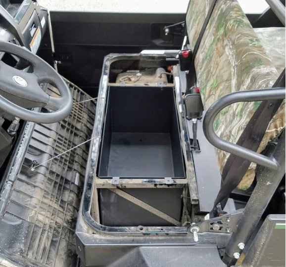 A Kawasaki Mule Pro with the passenger seat lifted to show a black Under Seat Storage Basket/Bin. The passenger seat features a camouflage pattern, while the floor appears dusty and the driver’s seat with steering wheel is visible.