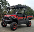 A red and black Mule Pro Fx Metal Top UTV with off-road tires, a protective front bumper with winch, overhead roof rack, and open cabin is parked on a paved road beside trees and greenery.