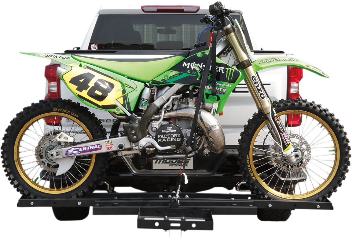 A green motocross bike with number 48, featuring Monster Energy branding, is securely mounted on a hitch carrier attached to the back of a white pickup truck. The bike’s tires and details are clearly visible against the clean truck background.