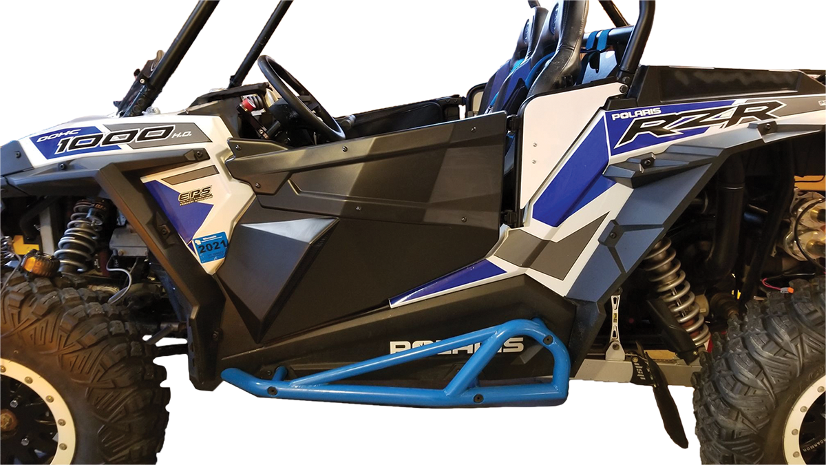 A close-up side view of a blue, white, and black Polaris RZR off-road vehicle, highlighting its rugged tires, suspension, roll cage, graphics, and blue rock slider, with the drivers seat and steering wheel partially visible.