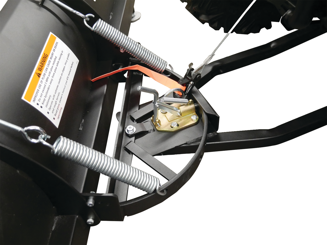 Close-up of a black metal snow plow attachment with silver springs, a yellow metal locking mechanism, warning label, and orange safety strap, mounted on a vehicle with visible tires and attachment arms against a white background.