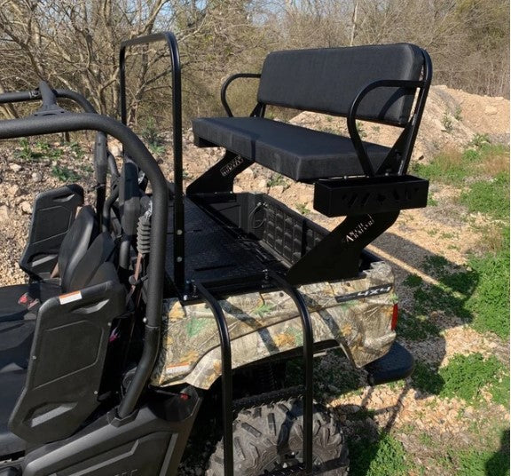 The Yamaha Viking High Seat, featuring a camouflage pattern, is mounted on the cargo bed with a black metal and cushioned bench, armrests, a backrest, and two ladder steps for access. The background shows trees and rocky terrain.